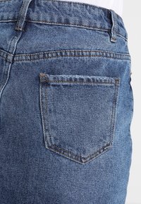Modré džíny z denimu s zadní kapsou, čistým prošitím a mírně vybledlou strukturou. Pas obsahuje poutka na opasek pro upevnění.