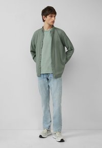 Jasnozielona koszula zapinana na guziki nałożona na miętową koszulkę, połączona z jasnoniebieskimi dżinsami i jasnymi trampkami. Minimalistyczny design i tekstury.