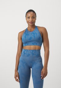 Sutiã desportivo azul e leggings de cintura alta com um padrão de camuflagem subtil. Feitos de um tecido texturizado e elástico. Apresenta um logótipo na parte da frente.