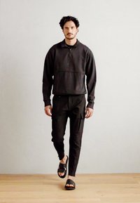 Svart quarter-zip genser med frontlomme, parret med svarte cargo-bukser og svarte sandaler, med en jevn tekstur og avslappet passform.