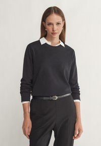 Marineblauw sweatshirt met ronde halslijn, lange mouwen en witte kraagdetails, gecombineerd met op maat gemaakte zwarte broeken en een zwarte riem.