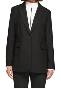 Svart skräddarsydd kavaj med en enkel knappstängning, spetsiga slag och två sidofickor, bärs över en vit höghalsad tröja.