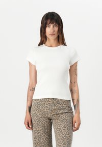 T-shirt bianco a maniche corte con scollo rotondo, silhouette aderente e texture liscia, abbinato a pantaloni a stampa leopardata.