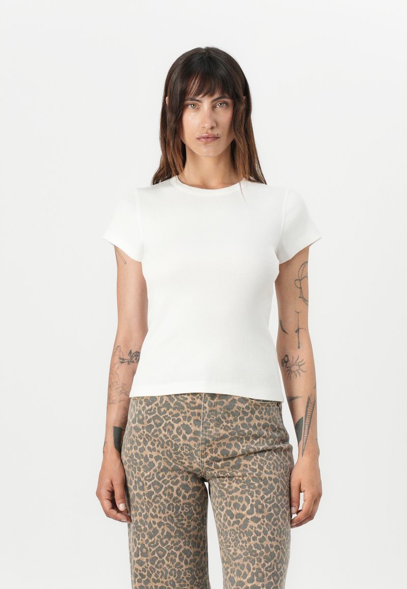 T-shirt bianco a maniche corte con scollo rotondo, silhouette aderente e texture liscia, abbinato a pantaloni a stampa leopardata.
