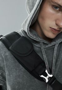 Szary hoodie o teksturowanym wyglądzie, z czarnym paskiem i srebrną klamrą. Materiał jest miękki, z widocznymi szczegółami przeszyć.