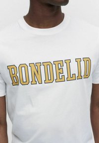 Vit bomullst-shirt med djärv guldfärgad och svart "BONDELID"-text över bröstet. Kortärmad, rund halsringning, mjuk textur.