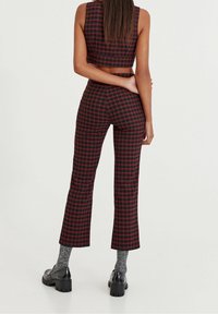 Top corto a quadri neri e rossi e pantaloni abbinati, sagomati con orlo svasato. L'insieme presenta una texture liscia e un design minimale.