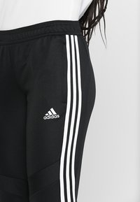 Black athletic pants with white three-stripe design along the sides, elastic waistband, and Adidas logo on the lower leg.