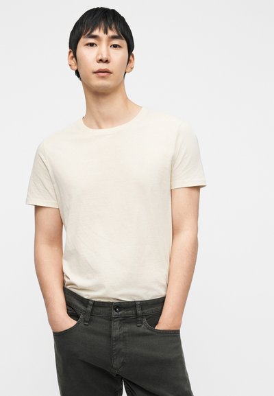 Μπεζ κοντομάνικη μπλούζα από μαλακό ύφασμα. Σκούρο πράσινο τζιν με κλασική γραμμή, διαθέτει τσέπες και κλείσιμο με κουμπί.