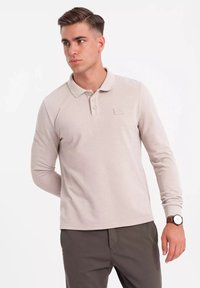 Polo a maniche lunghe beige in tessuto testurizzato, con colletto classico e tre bottoni. Presenta un piccolo logo impresso sul petto.