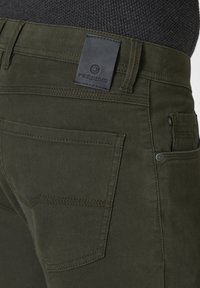 Dark green cotton pants featuring a black leather logo patch, two back pockets, and subtle stitching details.