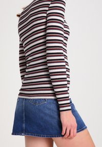 Randig långärmad topp i vitt, rött och marinblått, kombinerad med en blå denimminiskirt med utsvängd nederkant och bakfickor.