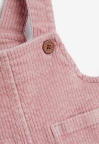 Rosa Corduroy-Latzhose mit horizontaler Rippung, einer quadratischen Fronttasche und einem braunen Knopf am Träger. Weicher Stoff und lässiges Design.