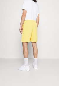 Shorts en coton jaunes avec une taille élastique, deux poches latérales, associés à un T-shirt blanc et des baskets blanches.