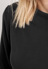Schwarzes Langarmtop mit glatter Textur. Das Design verfügt über einen Rundhalsausschnitt und minimale Nähte nahe der Schulter.