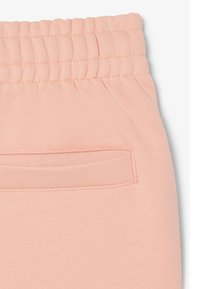 Roze elastische tailleband met een gestikte paspelzak op zachte stof, waarschijnlijk onderdeel van casual broeken of shorts.