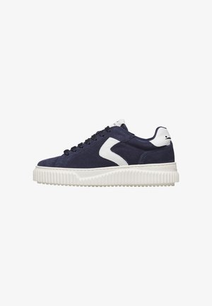 Navy suede sneaker with white zigzag detail, black laces, white padded heel and tongue, and thick textured white rubber sole.