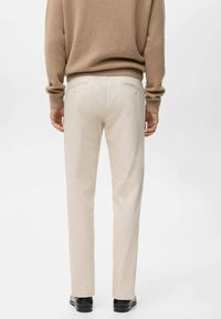 Pantalones beige a medida con un diseño de pierna recta, textura suave y detalles sutiles en las costuras. Combinados con un suéter marrón claro y zapatos negros.