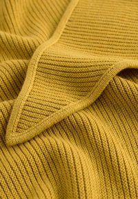 Gebreide stof in een goudgele tint met een getextureerd geribd patroon. De randen hebben een gladde, gestructureerde rand.