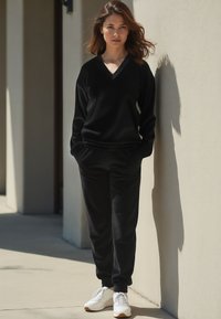 Felpa nera con scollatura a V e maniche lunghe, abbinata a pantaloni jogger coordinati. Il tessuto sembra morbido; abbinata a scarpe da ginnastica bianche.