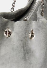 Borsa in suede grigia con hardware in argento, dotata di chiusura a zip e due chiusure decorative. Texture morbida e forma arrotondata.