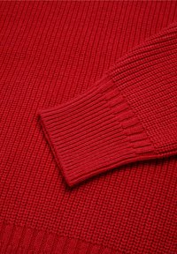 Suéter rojo de punto con puños y cuerpo acanalados, que presenta un patrón texturizado que destaca la calidez y comodidad.