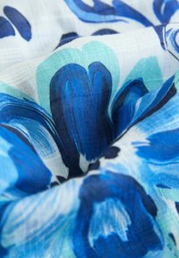 Bloemenstof met grote blauwe en aqua bloemblaadjes op een lichte achtergrond, met een zachte textuur en een subtiel geweven patroon.