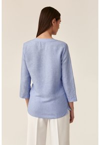 Blusa di lino azzurro chiaro con maniche a tre quarti, scollatura rotonda e spacchi laterali sull'orlo. Texture liscia con una sottile trama.