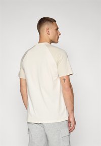 Lys beige kortermet t-skjorte med rund hals og raglanerm, laget av mykt stoff. Jevn tekstur med minimale detaljer.