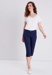 Marineblauwe gekorte broek van rekbare katoen, met een sluiting aan de voorkant met een knoop, achterzakken en zijsplitten aan de zoom. Geverfd met een witte V-hals shirt.