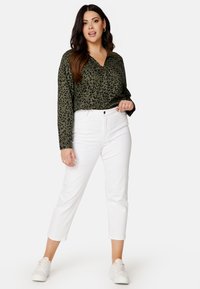 Blusa verde con stampa leopardata, con chiusura a bottoni, abbinata a pantaloni bianchi alla caviglia e sneakers bianche. Tessuto testurizzato, vestibilità rilassata.