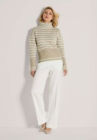 Beige- und weiß gestreifter Rollkragenpullover mit gerippter Textur. Kombiniert mit weißen, weit geschnittenen Hosen und neutralen, spitzen Absätzen.