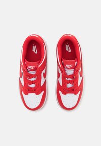 Red sneakers with white accents, round toe, mesh fabric, laces, and perforated toe box. Nike logo on side and tongue. Textured sole.