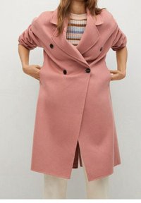 Lyserød uldblandings dobbeltradet frakke med store sorte knapper, brede revers og en afslappet pasform, lagdelt over en stribet sweater.