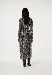 Schwarzes Langarmkleid mit einem detaillierten weißen Kreisdruck. Das Kleid fließt bis zur Mitte der Waden und wird mit schwarzen, glänzenden knielangen Stiefeln kombiniert.
