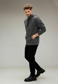 Sudadera gris con paneles texturizados en los hombros, bolsillos frontales, combinada con pantalones negros y botas negras con cordones. Diseño simple y ajuste cómodo.