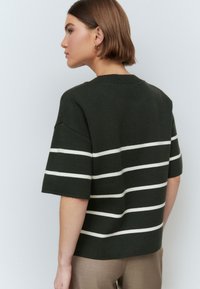 Pulover scurt cu maneci scurte, de culoare verde închis, cu dungi orizontale albe. Are un decolteu rotund și o croială lejeră, fiind realizat dintr-un material tricotat moale.