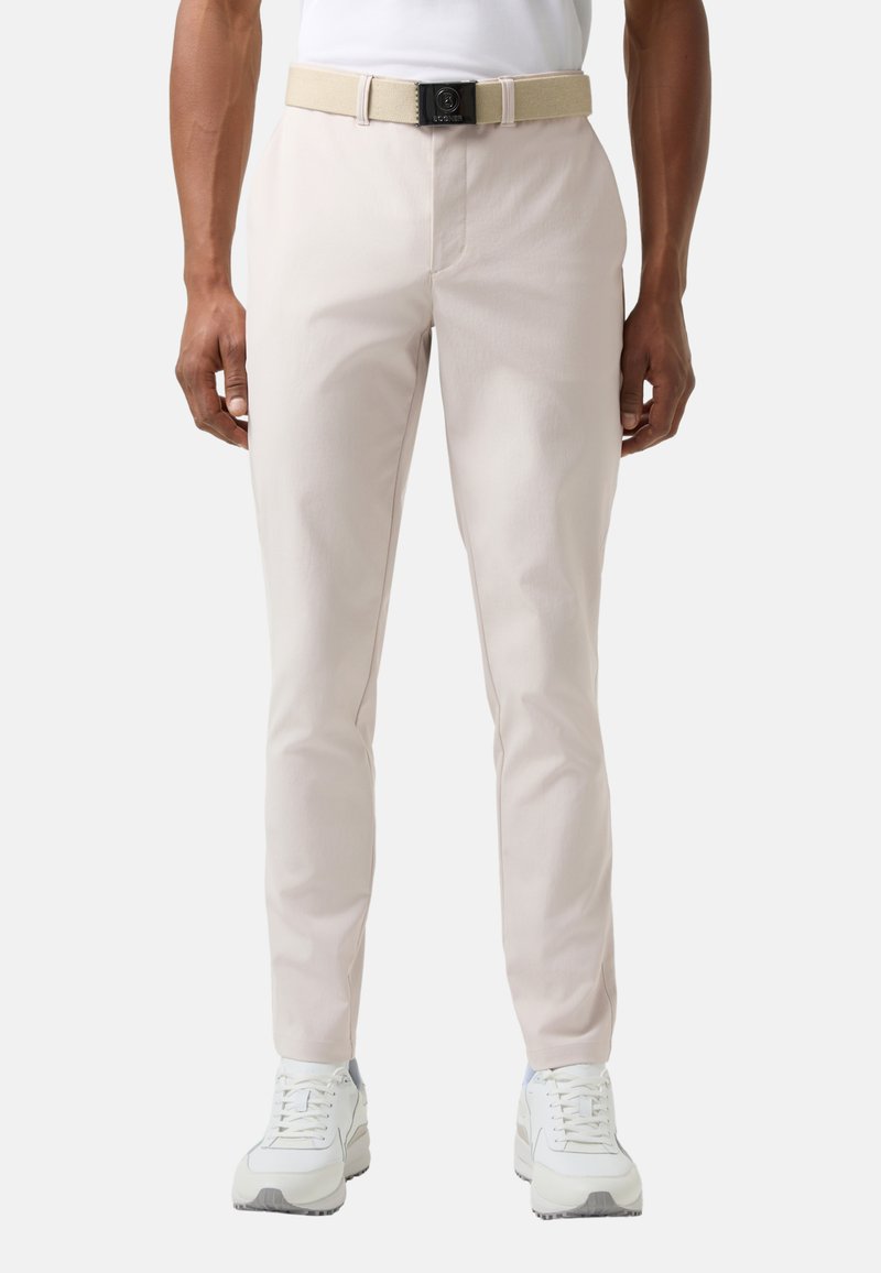Jasnobeżowe spodnie chino o wąskim kroju, wykonane z teksturowanej tkaniny, z szlufkami na pasek i dołączonym paskiem w tym samym kolorze. Noszone z białymi trampkami.
