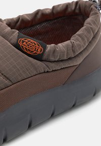 Brun Lacoste-sneaker med en strukturerad ovandel, elastisk krage och en hållbar svart gummisula med upphöjda accenter.