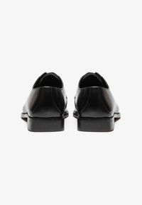 Zapatos de cuero negros con un acabado suave, punta redondeada y costuras mínimas, con un bajo tacón negro y diseño de talón abierto.