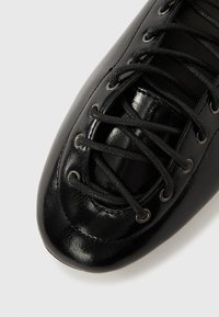 Fekete bőr cipő fényes felülettel, hagyományos fűzőkkel és kerek fémfülekkel. Áramvonalas kialakítás hegyes orr-résszel.