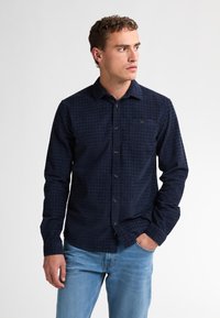 Marineblauwe langarmshirt met een geruit patroon, knoopsluiting aan de voorkant en een enkele borstzak. Gemaakt van een gestructureerde stof.
