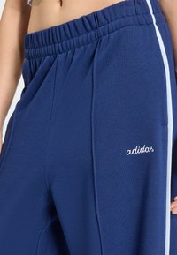 Marinblåa mjukisbyxor med resår i midjan, med en vit sidrand och broderad "adidas"-logotyp på vänster ben. Mjuk tygstruktur.
