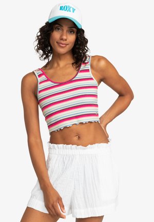 Haut court rayé en rose, bleu et blanc avec un ourlet festonné, associé à un short blanc à taille haute texturé. Casquette blanche avec le logo "ROXY".