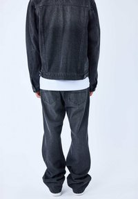 Chaqueta de mezclilla negra con un corte relajado, costuras en contraste y una camisa blanca por debajo. Pantalones de mezclilla negros holgados con bolsillos traseros.