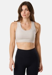 Soutien-gorge de sport beige avec un encolure ronde et des bretelles larges, présentant une texture solide et une bande logo en relief, associé à un legging noir taille haute.
