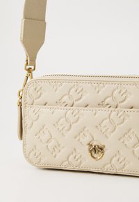Beige neplederen schoudertas met reliëf bloemenpatronen, gouden beslag en een afneembare strap met een gladde textuur.