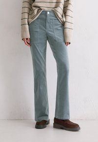 Licht tealkleurige corduroy broek met uitlopende benen, voorzien van voorzakken en een platte voorkant met een enkele knoopsluiting.