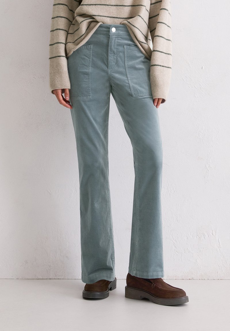 Licht tealkleurige corduroy broek met uitlopende benen, voorzien van voorzakken en een platte voorkant met een enkele knoopsluiting.