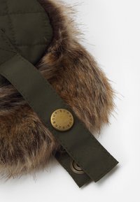 Material quilted verde cu tiv din blana sintetica maro. Prezinta un buton auriu cu inscripția "BARBOUR" gravata si un orificiu pentru fixarea curelei.